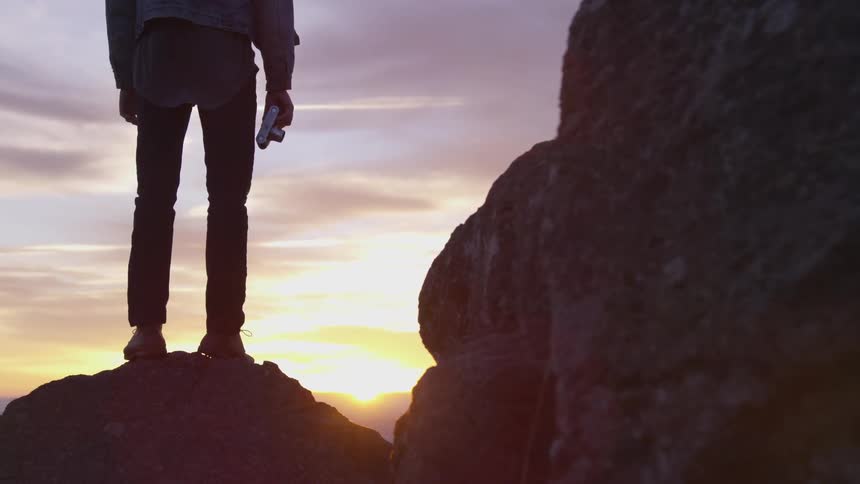 Man stands on rock holding a camera at sunset