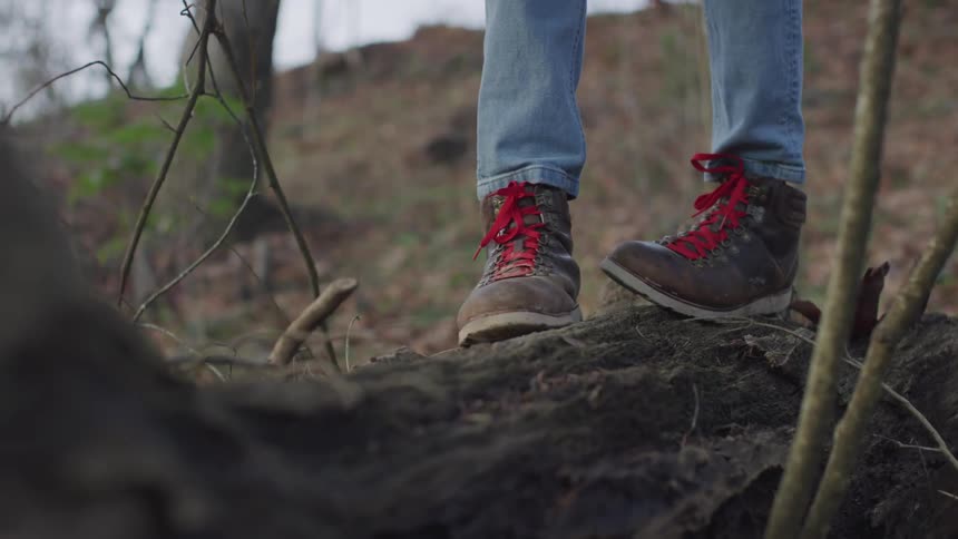 Person in hiking boots crosses fallen tree stump on grassy hill