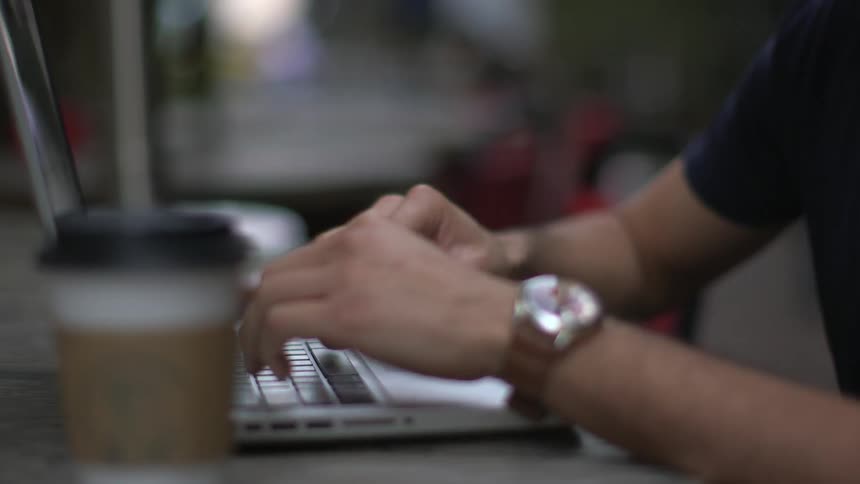 Man using a laptop takes a drink from a beverage