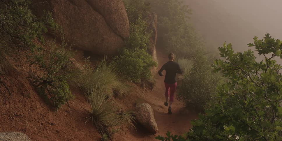 A woman running/jogging on a rocky trail in the fog