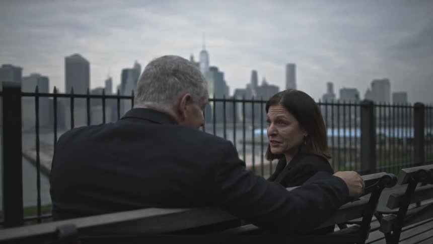 Man and woman sit on a bench by the water talking on a cloudy day