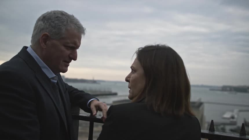 An elderly couple converse on a bridge overlooking the city