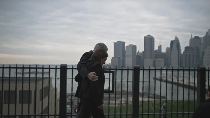 Man and woman walking along a railing with a city in the background
