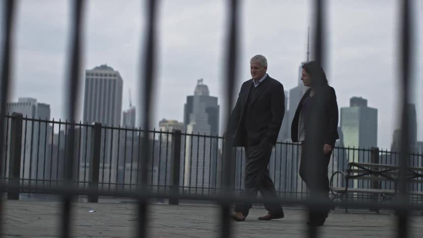 Man and woman walk with a city behind them on a cloudy day