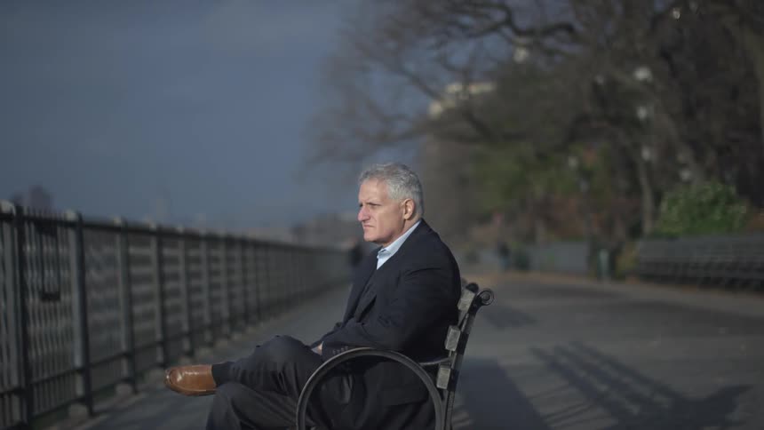 A mature man, wearing a leisure suit, sits alone on a park bench