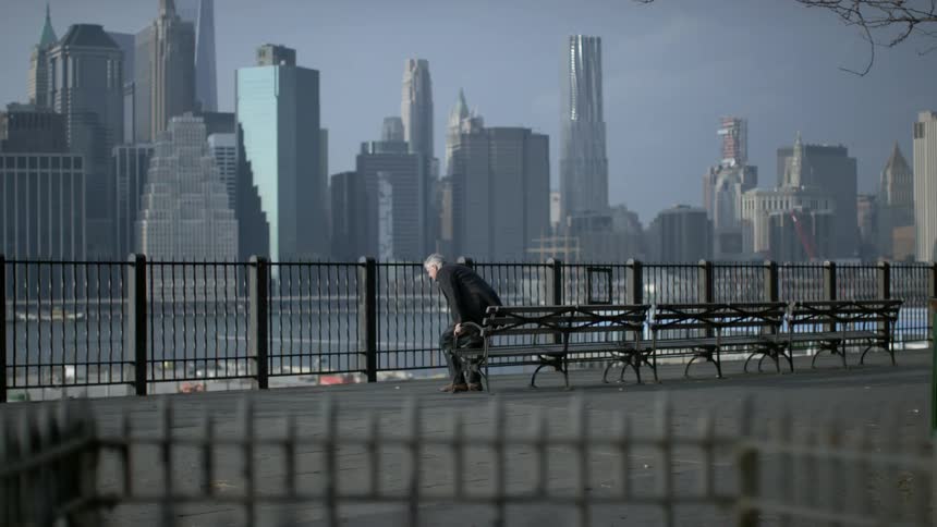 Man sitting on bench overlooking city stands up and walks away