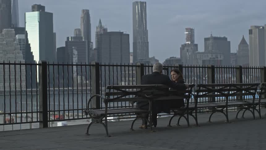 Two people sitting on a bench overseeing a city on a cloudy day