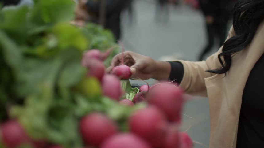 People walking past a sidewalk market examining vegetables