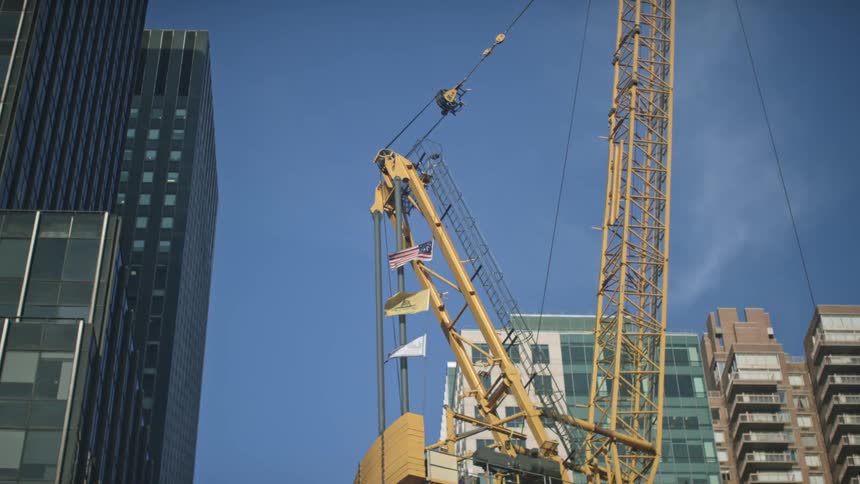 A large yellow crane turns near a building