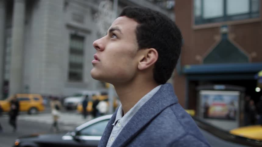 A man stands on a city street looking up at the sky