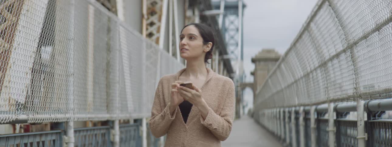 Middle eastern woman walking across bridge while she looks at phone