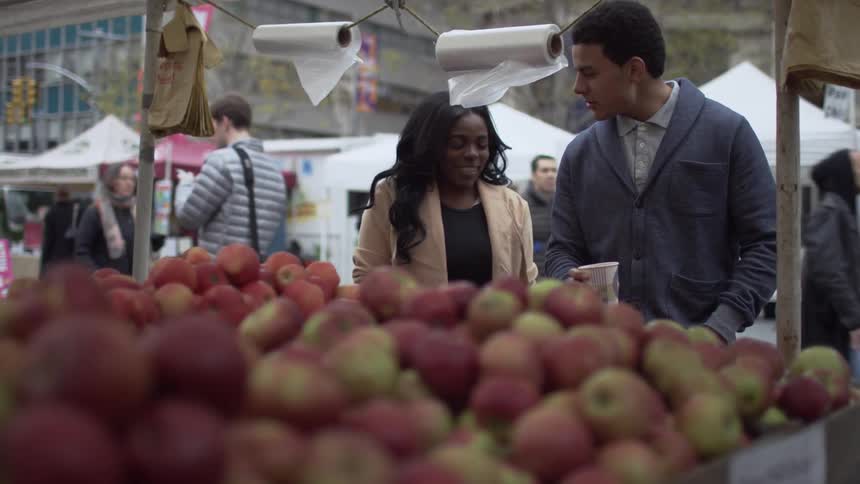 Man and woman converse while shopping for produce in a market outdoors