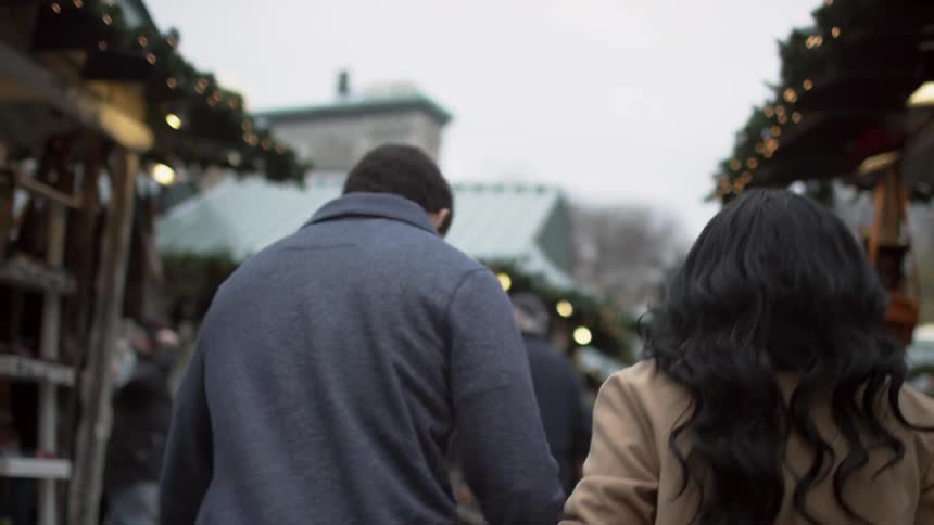 A couple walk through a city market on an overcast day while holding hands
