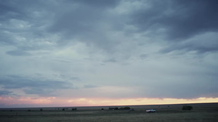 A truck drives down a country road at sunset on a cloudy day