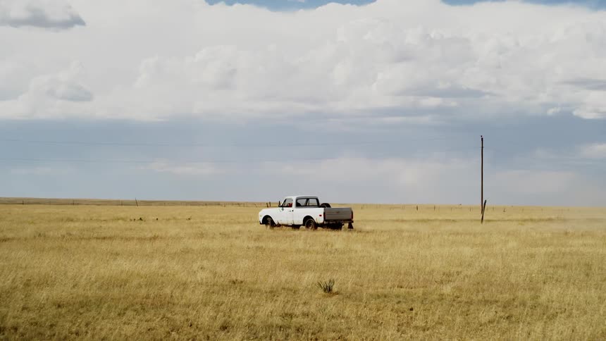 A white truck travels down a dirt field on a cloudy day