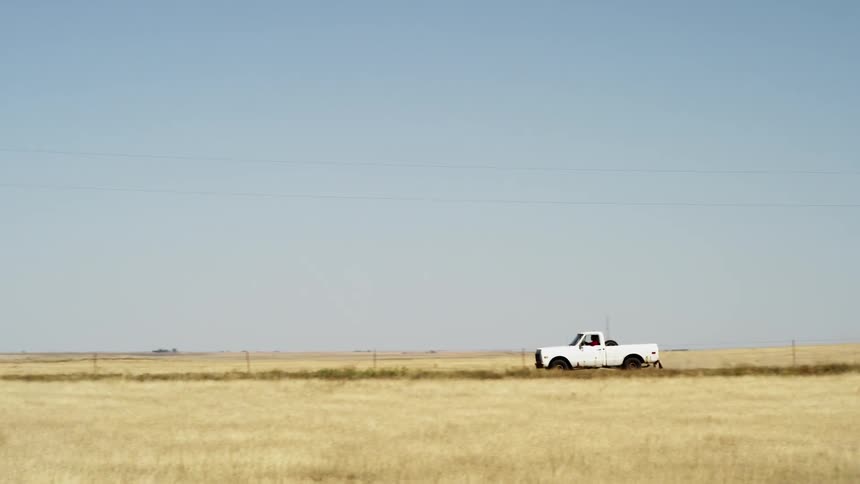 A white truck rides down a road between two fields