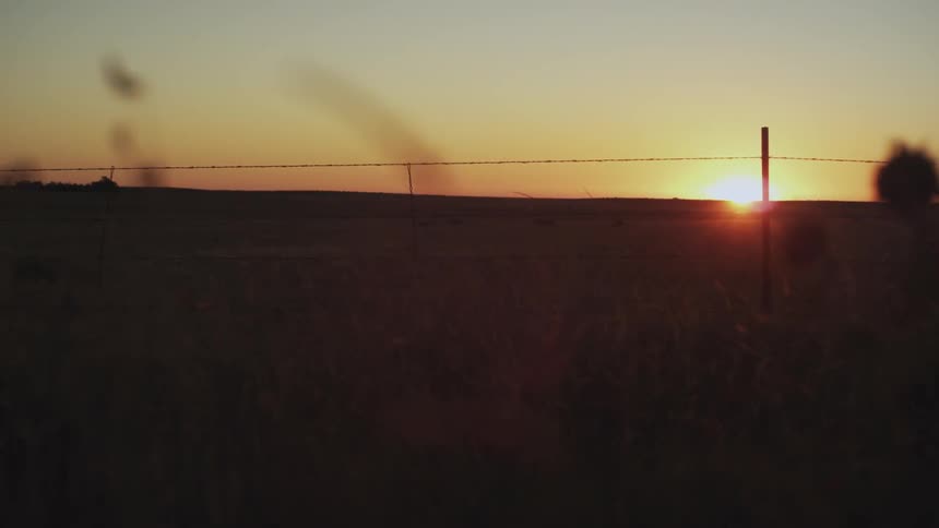 The sun is setting over a ridge as seen from a grassy field