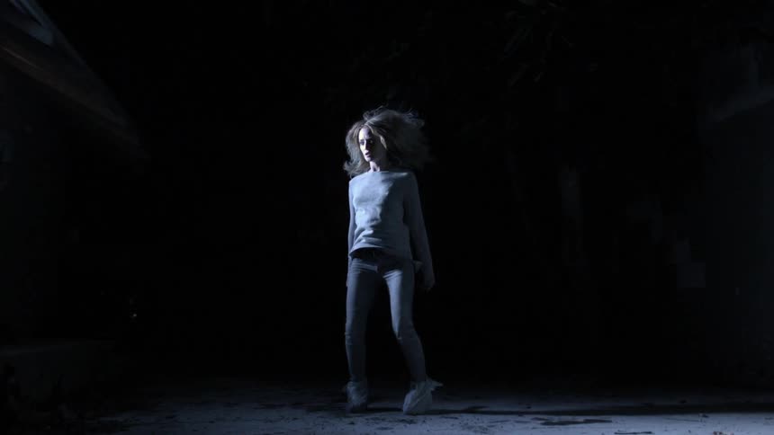 A woman slowly landing in a dark room