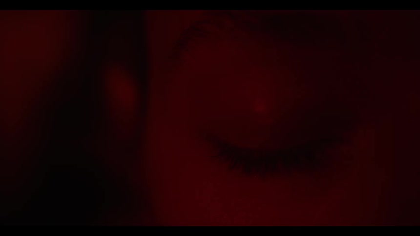 A woman stands with eyes shut as colors project behind her in a dark room