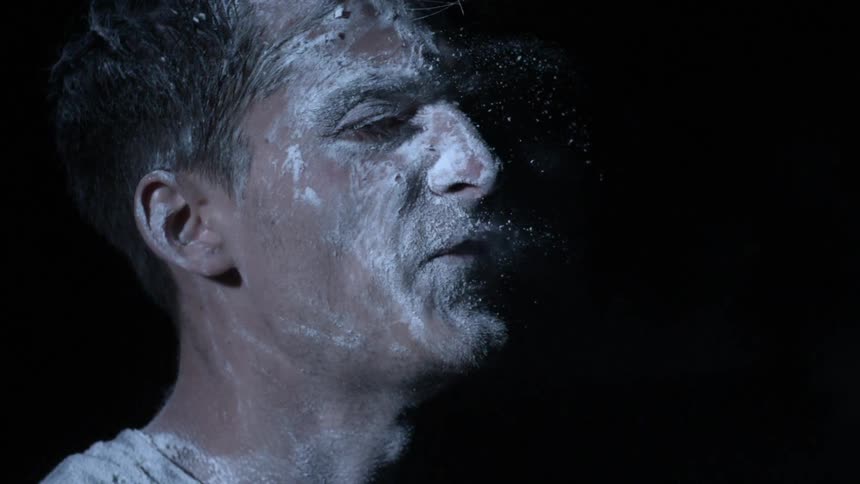 A man with white powder covering his face turns and yells