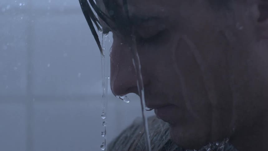 Man stands with his eyes closed as water pours on him