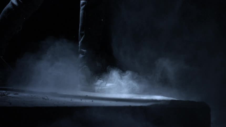 Dust swirls around a persons feet in a dark room with a single spotlight