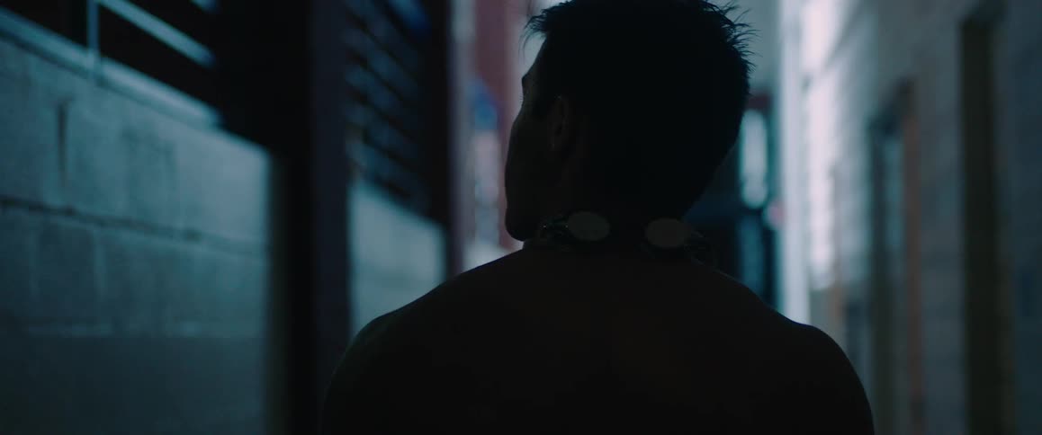 Man walks down a dim hallway while swimming goggles rest on his neck