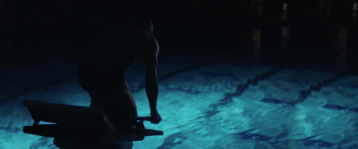A man getting ready to dive into a pool in a darkened gym