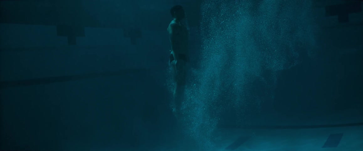 A man pushing up from the bottom of a pool in a dark area