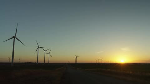 Wind turbines run on a large field as the sun sets