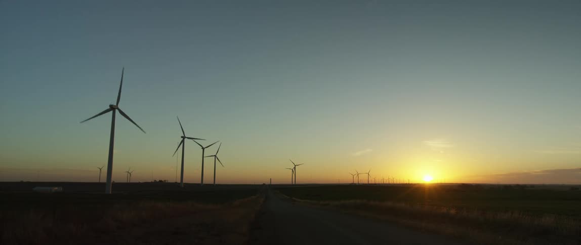 Wind turbines run on a large field as the sun sets