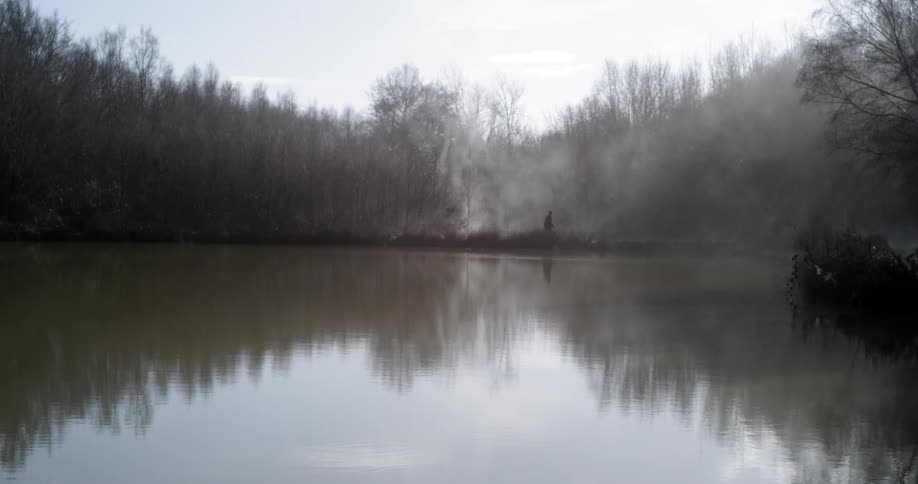 A person walking next to a foggy lake