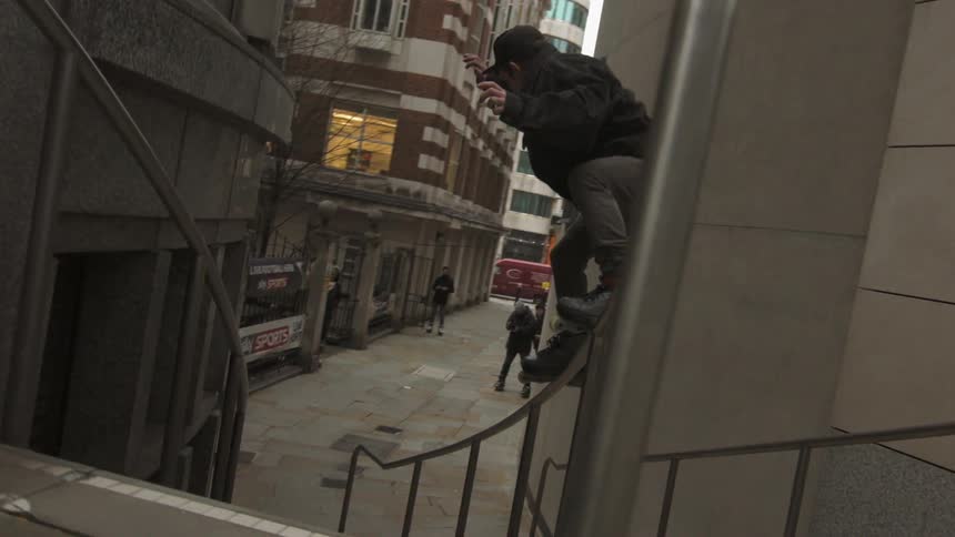 A guy with roller skates on is jumping down a flight of stairs between two buildings