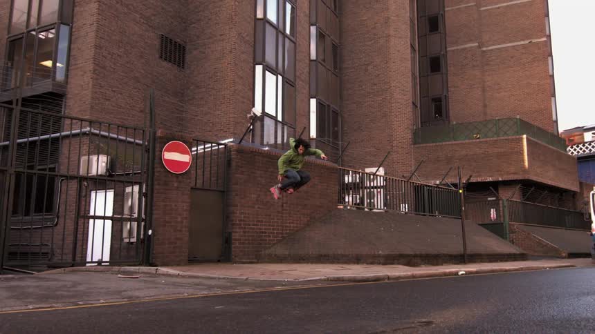A man performs a grinding trick while rollerblading against a brick building