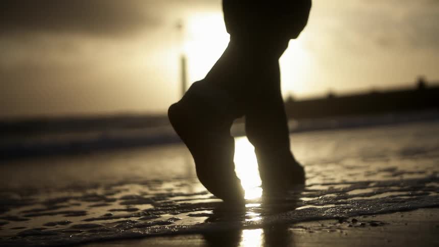 A man walks along the shoreline at sunset