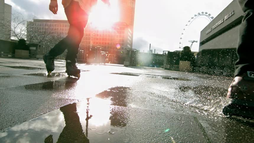 Slow motion clip of two people rollerblading on asphalt after a rain shower