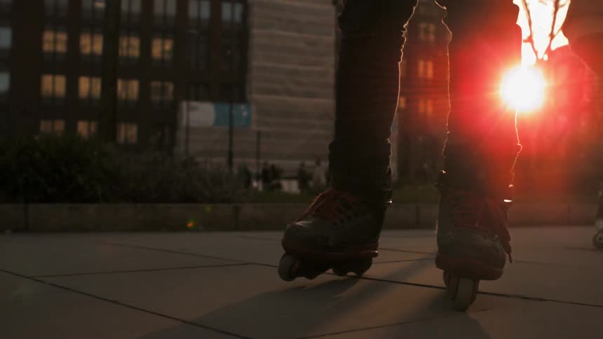 Close up of people's legs and feet as the roller blade in an urban area at dusk