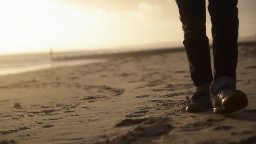 Person walking along the beach wearing shoes at sunset