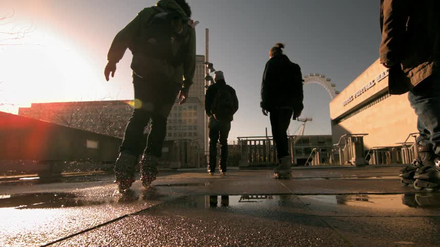 Three people rollerblade down a damp city street