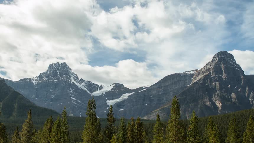 Timelapse of white clouds moving over tall mountains during the day