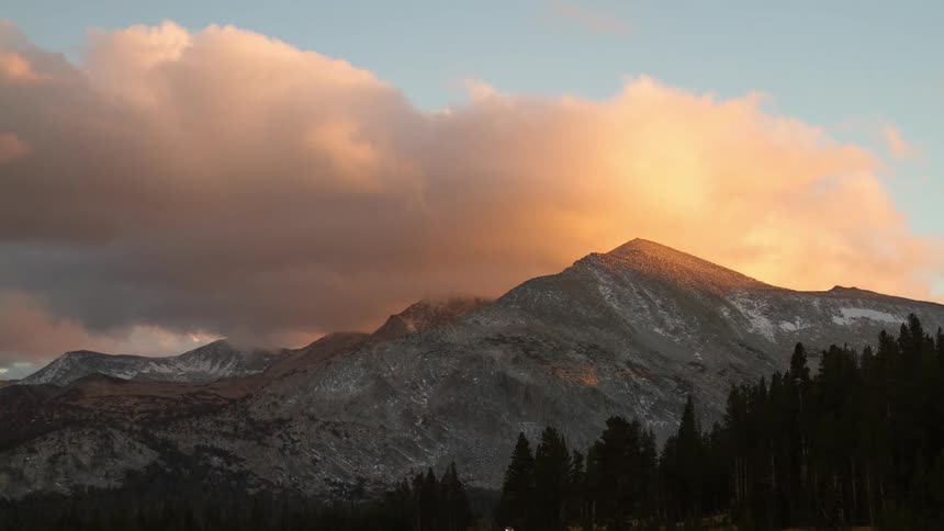 Clouds flow over a snowy mountaintop during the daytime