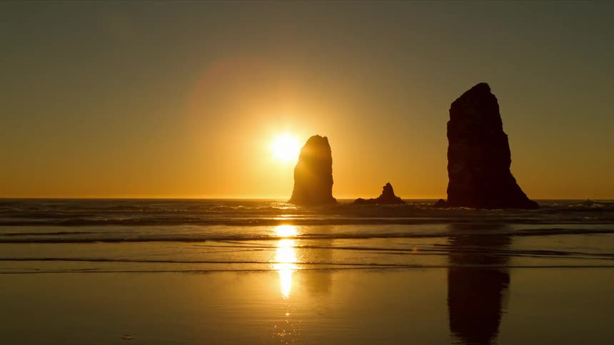 Time lapse of an ocean with two large rocks pointing out as the sun sets