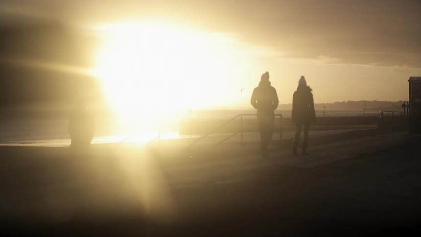 Two people walking as the sun rises by the water