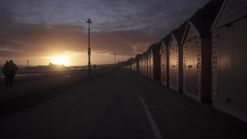 A long row of small sheds stand by a cloudy sky at sunset