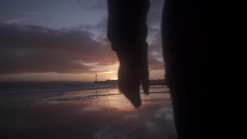 A man walks down a beach at sunrise