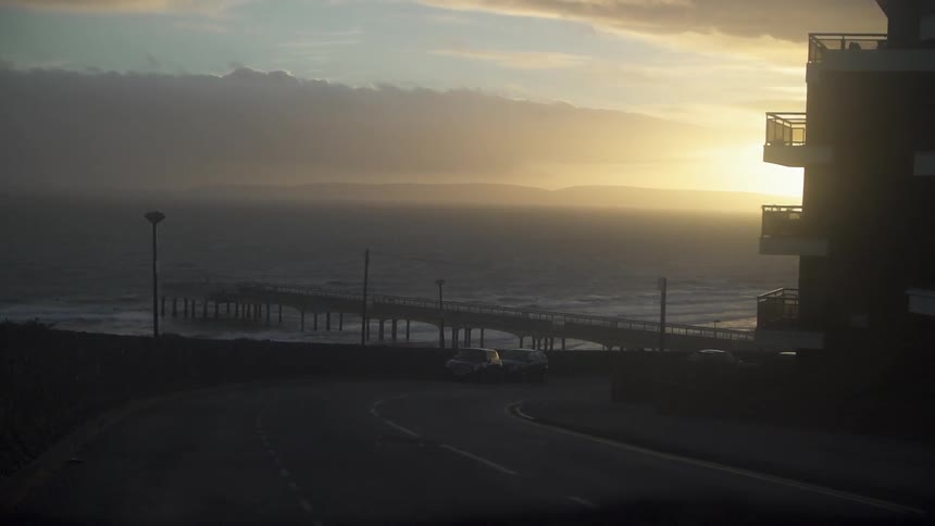 View looking down a curving street towards the ocean as the sun sets
