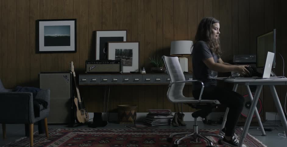 A young woman walks and sits at a desk after flinging a towel across the room