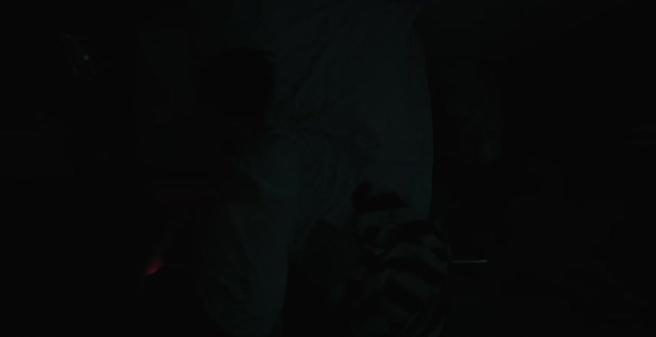 A young man laying in the dark watching something on his cell phone suddenly darts out of bed
