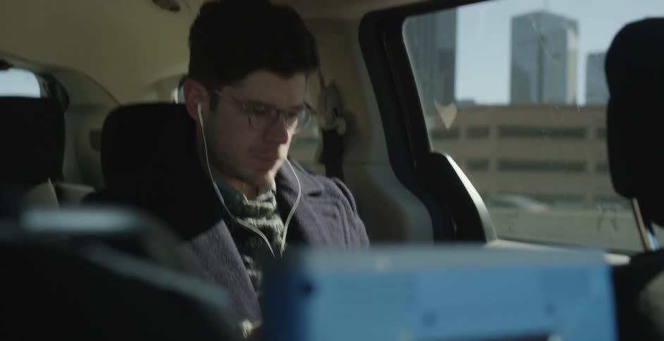 A man wearing earbuds sits in a van commuting