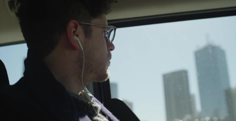 Man wearing earphones sits on a bus looking out the window